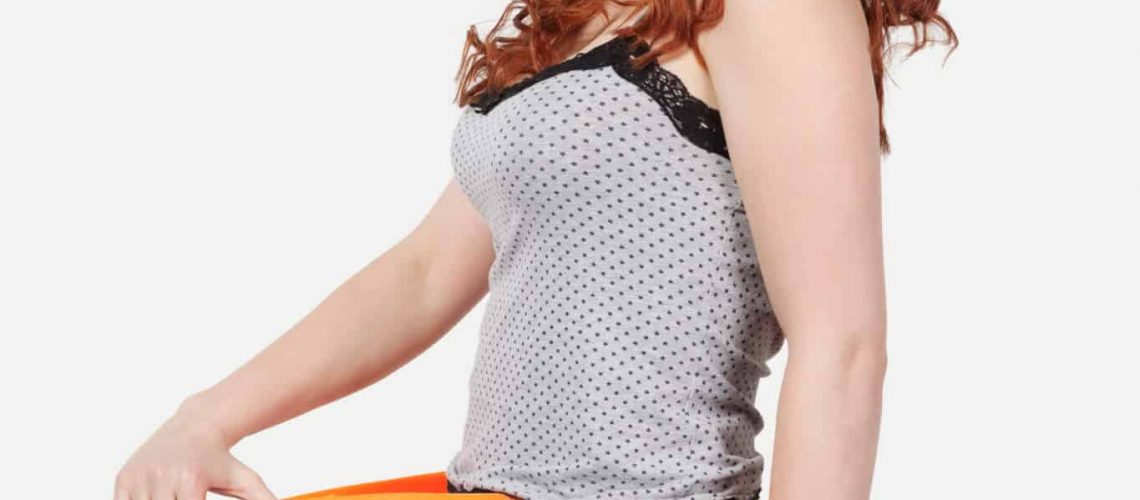 Portrait of young Caucasian woman oversized orange pants against gray background